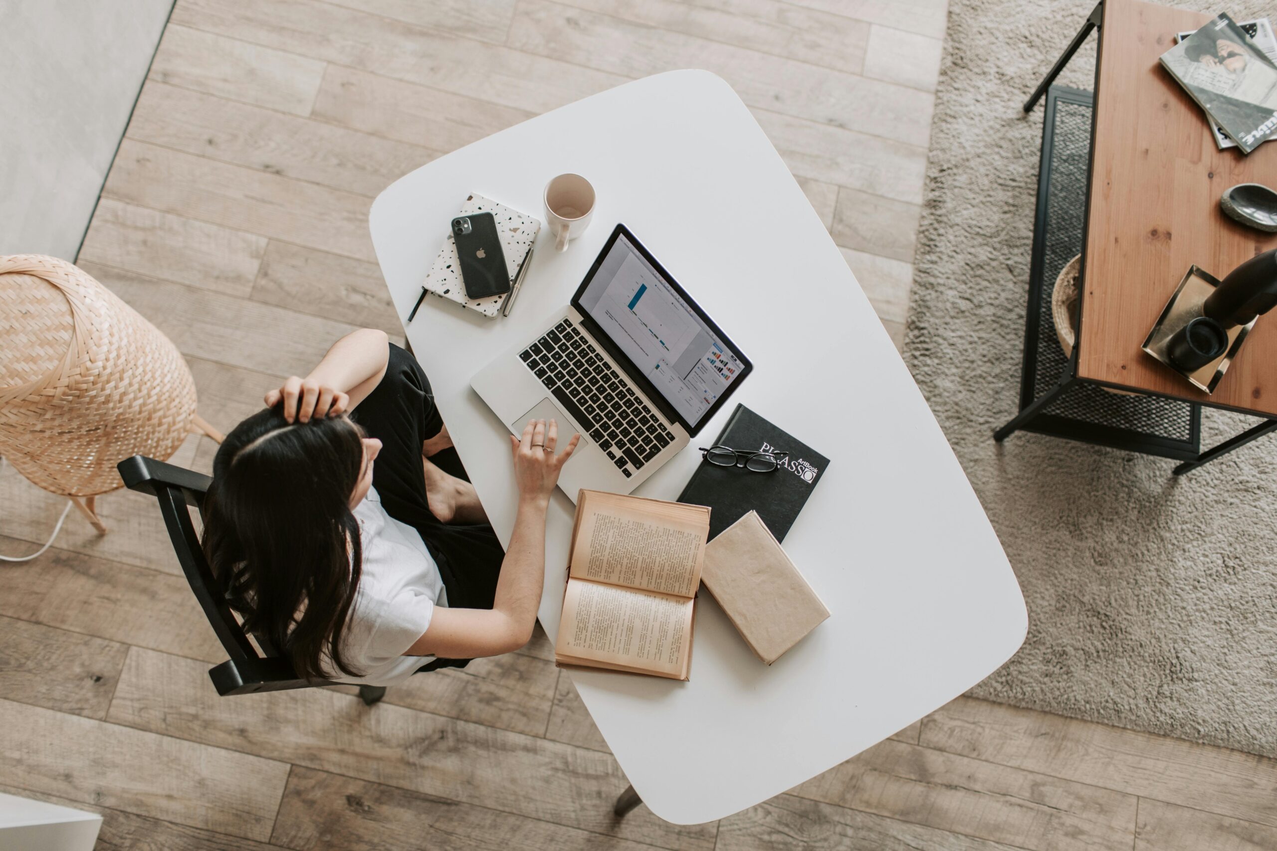 Servicios From above of young woman with long dark hair in casual clothes working at table and browsing netbook while sitting in modern workplace and touching hair